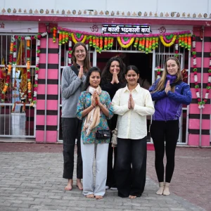 A group of yoga students standing in prayer pose (Namaste) outside a traditional Indian temple during an excursion as part of the 200 hour Kundalini yoga teacher training in Rishikesh.