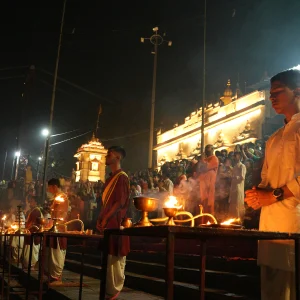 Priests and devotees performing the spiritual evening Ganga Aarti ceremony with oil lamps along the banks of the Ganges River during the 200 hour Kundalini yoga teacher training in Rishikesh.