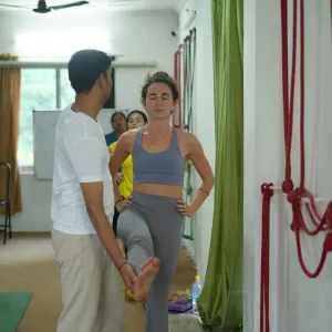 Yoga instructor guiding a female student through leg stretch posture adjustments during a 300 hour yoga teacher training in rishikesh session in a well-equipped studio.