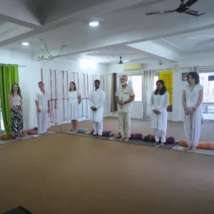 Yoga students wearing traditional white clothing standing together in a spacious studio during the opening ceremony of a 300 hour yoga teacher training in rishikesh.