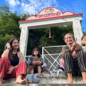Group of happy yoga students sitting on steps outside Kunjapuri Devi temple shrine entrance during a weekend excursion in a 300 hour yoga teacher training in rishikesh.
