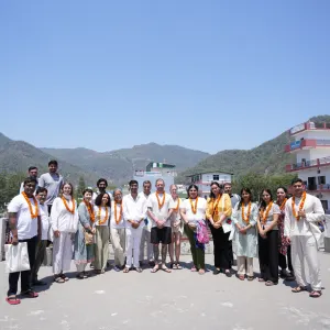 Large group of international yoga students and teachers wearing marigold garlands posing together on a rooftop with Himalayan mountains in the background during a 500 hour yoga teacher training in rishikesh.