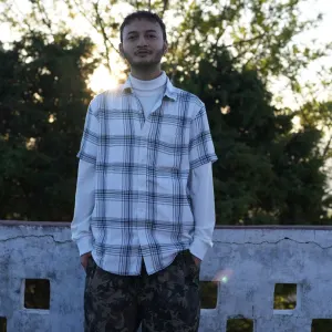 Outdoor portrait of a male student wearing a plaid shirt standing against a natural green backdrop during a 500 hour yoga teacher training in rishikesh.