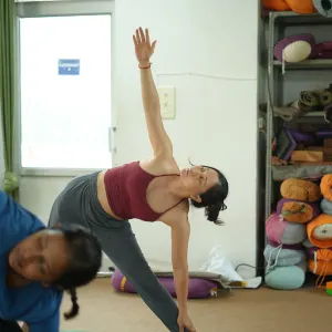 Female yoga practitioner performing Extended Triangle Pose (Trikonasana) with proper alignment inside a studio equipped with props during a 500 hour yoga teacher training in rishikesh class.