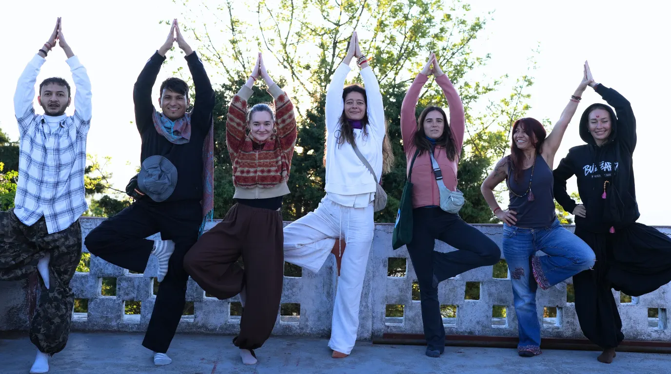 A group of practitioners performing tree pose outdoors during a 7 days yoga retreat in Rishikesh.