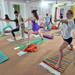 Rohit Kamboj demonstrating Warrior Pose while students practice Hatha Yoga in Rishikesh