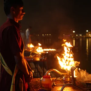 Young priest standing near a burning fire lamp during evening Ganga Aarti during an aerial yoga teacher training in Rishikesh.