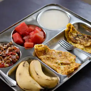 Healthy sattvic meal tray with fresh fruits, chana chat, and omelette served during aerial yoga teacher training in Rishikesh.