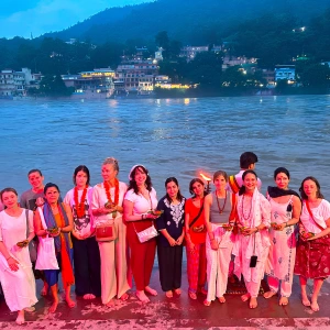 A group of yoga students gathered by the Ganges River at dusk during an aerial yoga teacher training in Rishikesh.