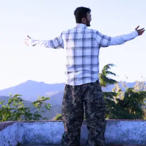 Man standing on a rooftop with open arms facing the Himalayan mountains during an aerial yoga teacher training in Rishikesh.