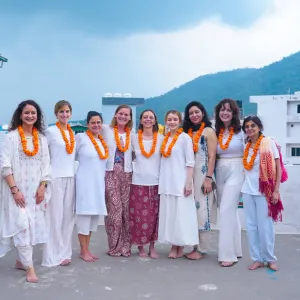 Group of yoga students wearing marigold garlands and traditional white attire during an aerial yoga teacher training in Rishikesh.