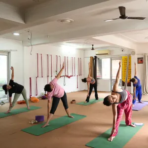 Yoga students practicing triangle pose in a spacious hall during an aerial yoga teacher training in Rishikesh.