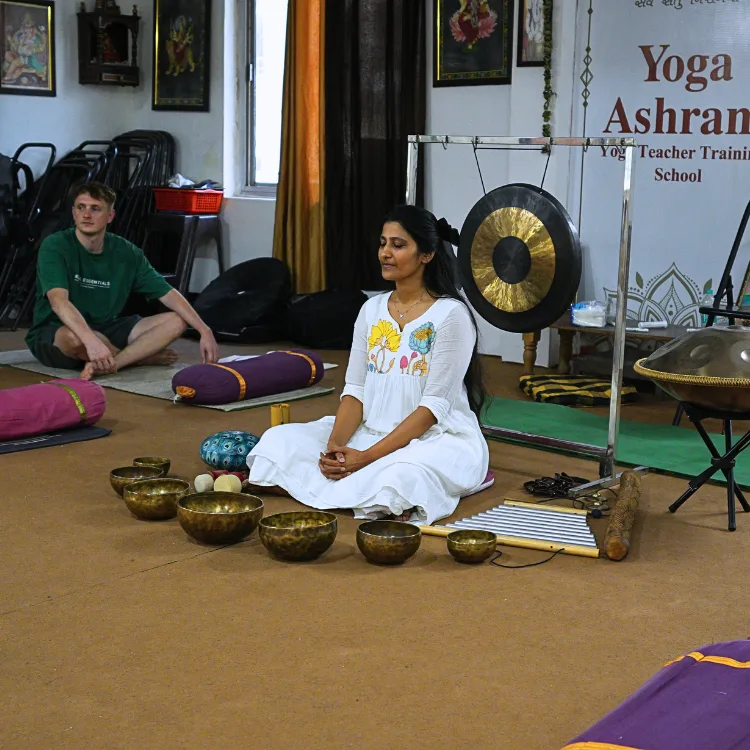 A woman meditating surrounded by Tibetan singing bowls, gongs, and handpans during a sound healing course in Rishikesh.