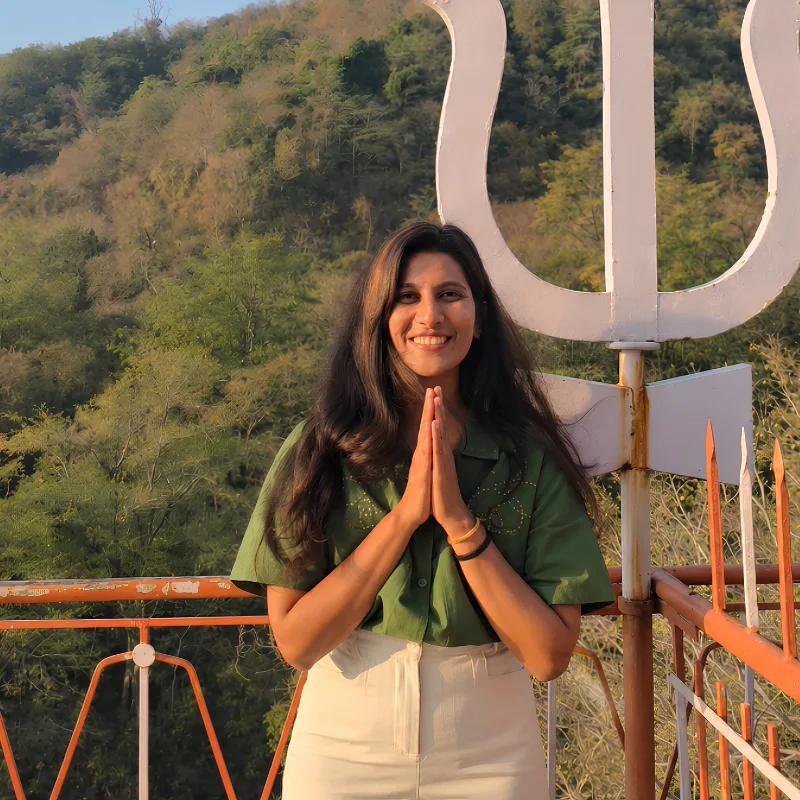 Ayushi Desai greeting with Namaste in a green shirt at a scenic hillside location in Rishikesh, India