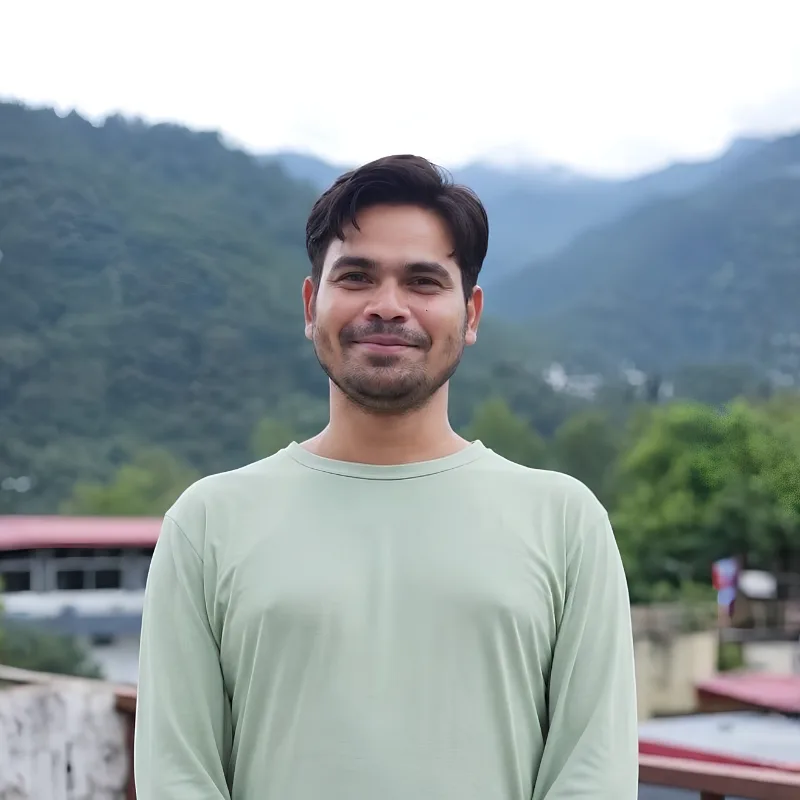 Rakesh Ji, yoga training course teacher in Rishikesh, India, standing outdoors against a Himalayan mountain backdrop