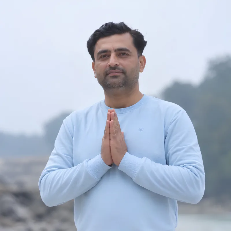 Rohit Kamboj, yoga training course teacher in Rishikesh, India, greeting with Namaste against a natural mountain backdrop
